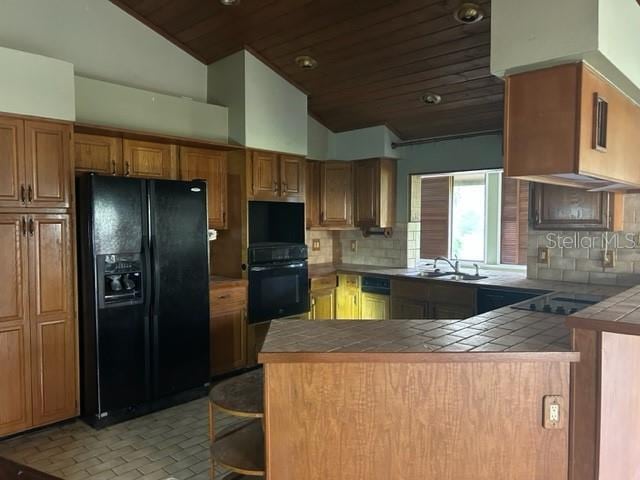 kitchen featuring decorative backsplash, tile countertops, kitchen peninsula, black appliances, and vaulted ceiling