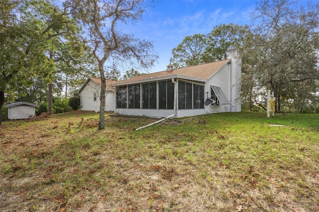 back of property with a sunroom, a storage unit, and a lawn