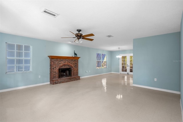 unfurnished living room with ceiling fan with notable chandelier, french doors, and a fireplace