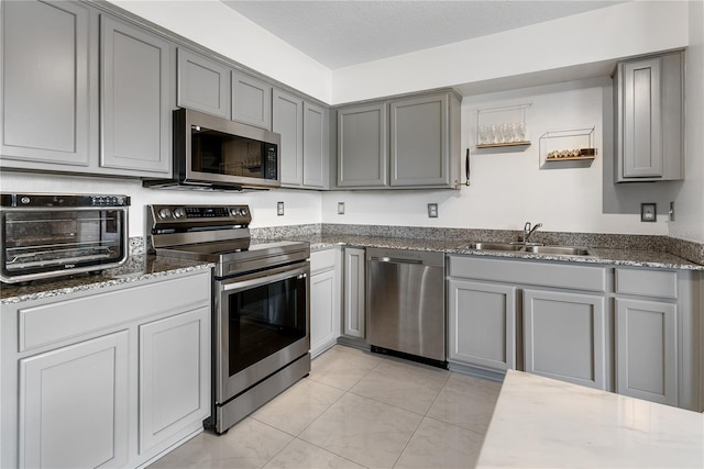 kitchen featuring appliances with stainless steel finishes, dark stone counters, sink, and gray cabinetry