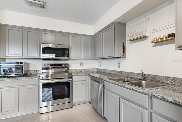 kitchen with a textured ceiling, sink, gray cabinetry, light tile patterned floors, and appliances with stainless steel finishes