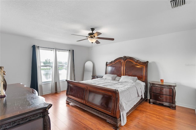 bedroom with a textured ceiling, light hardwood / wood-style floors, and ceiling fan