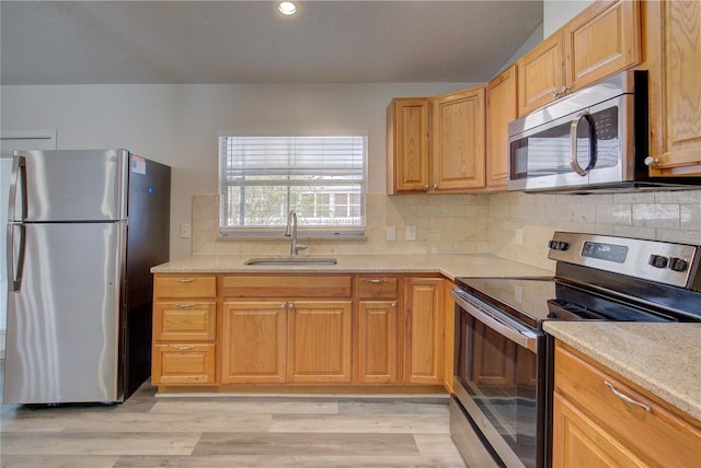 kitchen featuring backsplash, sink, light stone countertops, appliances with stainless steel finishes, and light hardwood / wood-style floors