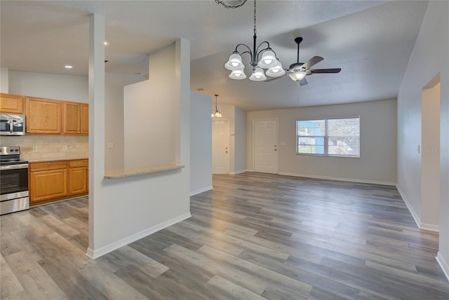 kitchen with light wood-type flooring, backsplash, stainless steel appliances, vaulted ceiling, and decorative light fixtures