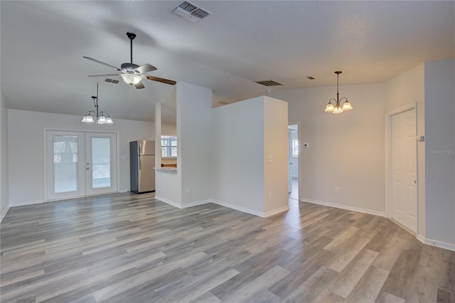 unfurnished living room featuring lofted ceiling, french doors, ceiling fan with notable chandelier, a textured ceiling, and light hardwood / wood-style floors