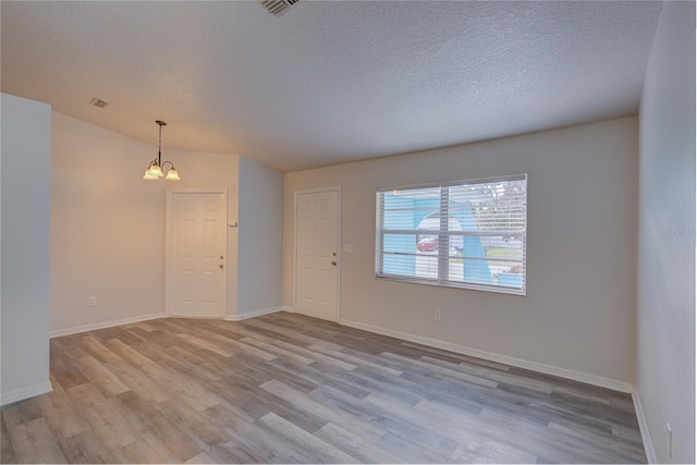 empty room featuring light hardwood / wood-style floors, a textured ceiling, and an inviting chandelier