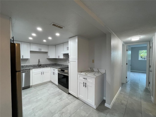 kitchen with appliances with stainless steel finishes, light stone counters, a textured ceiling, sink, and white cabinets