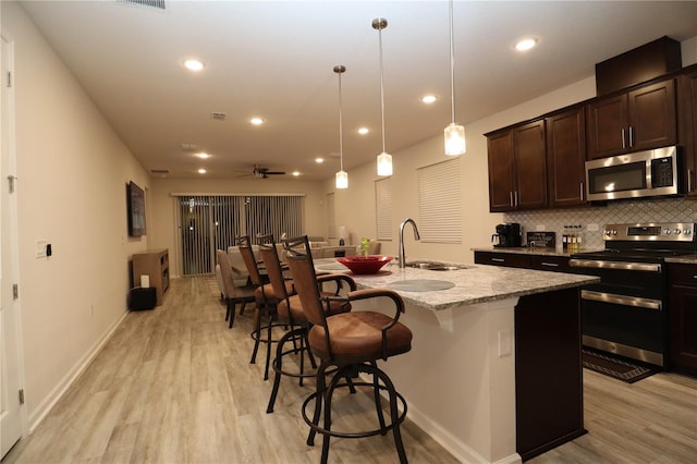 kitchen with decorative light fixtures, light stone countertops, stainless steel appliances, and a center island with sink