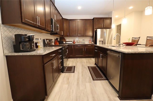 kitchen featuring sink, light wood-type flooring, stainless steel appliances, pendant lighting, and decorative backsplash