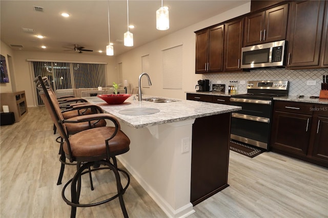 kitchen featuring appliances with stainless steel finishes, light stone counters, a kitchen island with sink, and light hardwood / wood-style floors