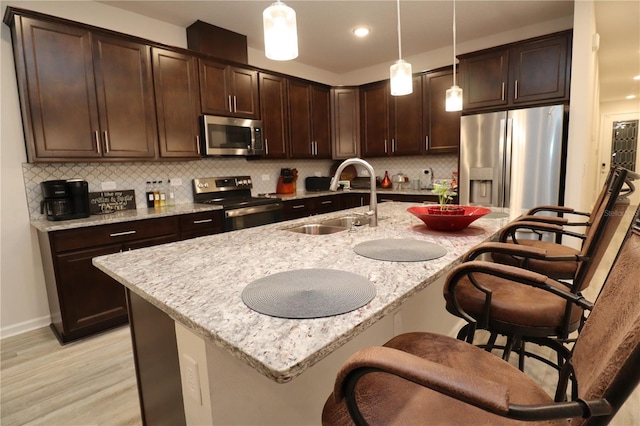 kitchen featuring sink, backsplash, hanging light fixtures, stainless steel appliances, and light hardwood / wood-style flooring