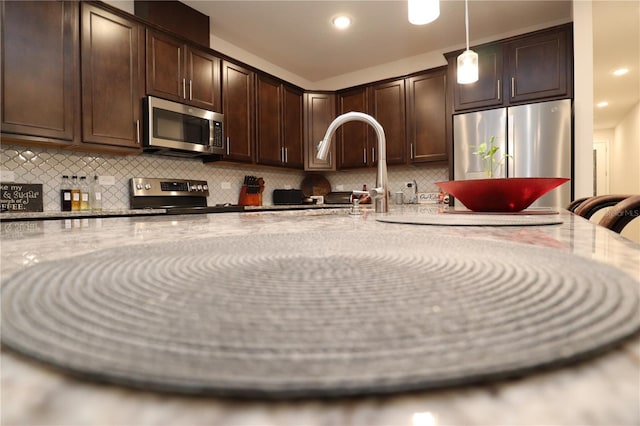 kitchen featuring dark brown cabinetry, hanging light fixtures, stainless steel appliances, and backsplash