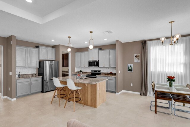 kitchen featuring a kitchen island with sink, hanging light fixtures, gray cabinetry, stainless steel appliances, and light stone counters