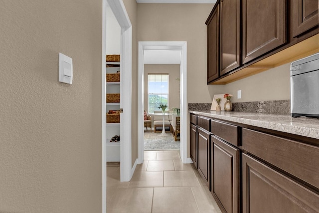 kitchen featuring light stone countertops, light tile patterned flooring, and dark brown cabinets