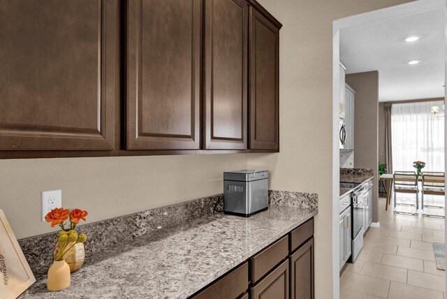 kitchen with appliances with stainless steel finishes, light stone counters, dark brown cabinets, and light tile patterned floors