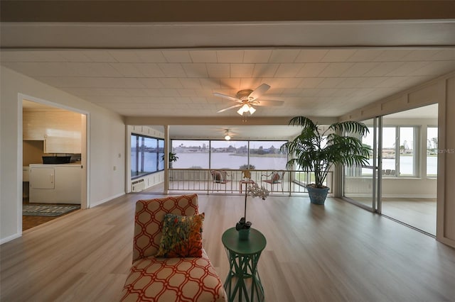 living room featuring separate washer and dryer, a water view, ceiling fan, and wood-type flooring