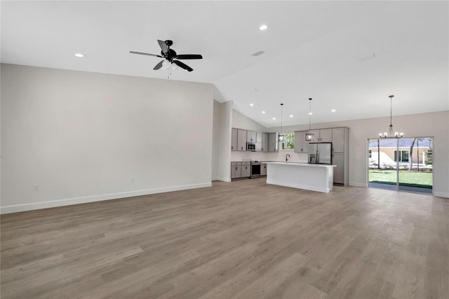 unfurnished living room featuring lofted ceiling, light wood-type flooring, and ceiling fan with notable chandelier