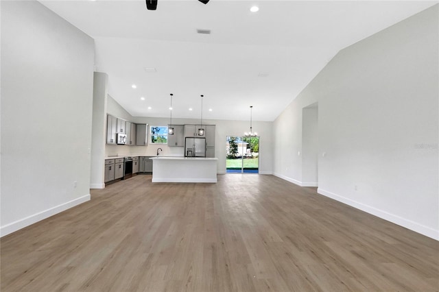 unfurnished living room with light hardwood / wood-style flooring, ceiling fan with notable chandelier, and vaulted ceiling