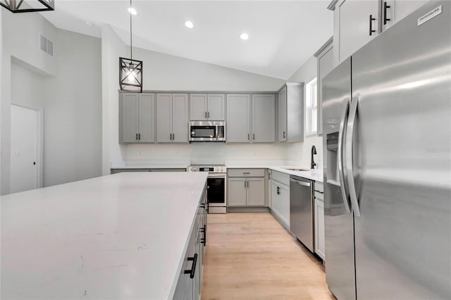 kitchen featuring lofted ceiling, gray cabinets, appliances with stainless steel finishes, pendant lighting, and light hardwood / wood-style floors