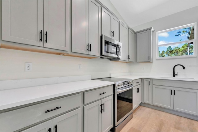 kitchen with light hardwood / wood-style flooring, gray cabinetry, sink, vaulted ceiling, and appliances with stainless steel finishes