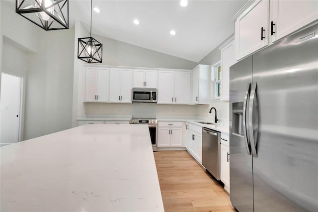 kitchen with hanging light fixtures, stainless steel appliances, sink, vaulted ceiling, and white cabinetry