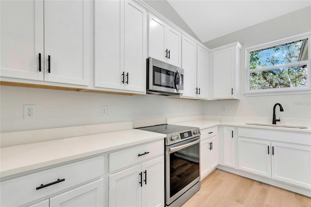 kitchen featuring lofted ceiling, light hardwood / wood-style flooring, sink, white cabinets, and appliances with stainless steel finishes