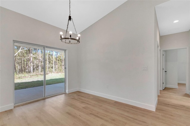 spare room with high vaulted ceiling, light hardwood / wood-style flooring, and an inviting chandelier