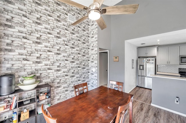 dining space with ceiling fan, wood-type flooring, and a high ceiling