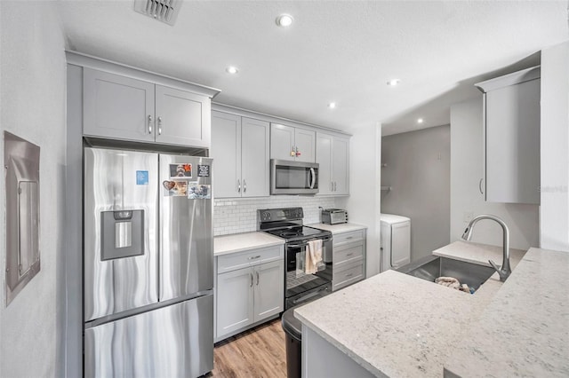 kitchen featuring washer and clothes dryer, sink, light wood-type flooring, tasteful backsplash, and stainless steel appliances