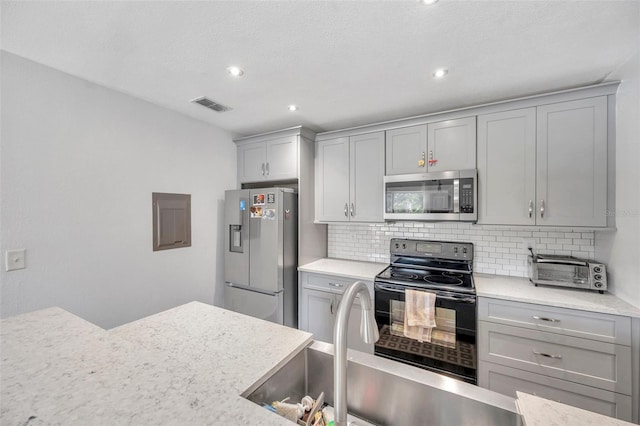 kitchen featuring decorative backsplash, light stone counters, gray cabinetry, stainless steel appliances, and sink