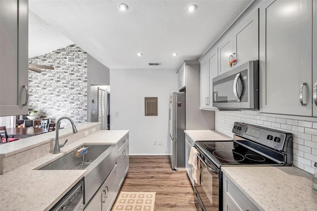 kitchen with light wood-type flooring, a textured ceiling, stainless steel appliances, sink, and lofted ceiling