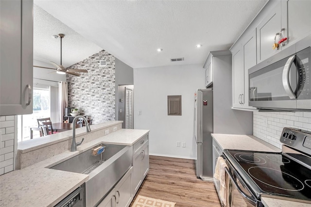 kitchen featuring light wood-type flooring, a textured ceiling, stainless steel appliances, sink, and lofted ceiling