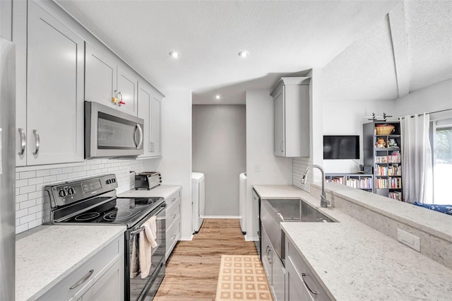 kitchen with separate washer and dryer, light stone counters, black / electric stove, light hardwood / wood-style floors, and decorative backsplash