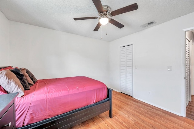 bedroom with a textured ceiling, a closet, light hardwood / wood-style flooring, and ceiling fan