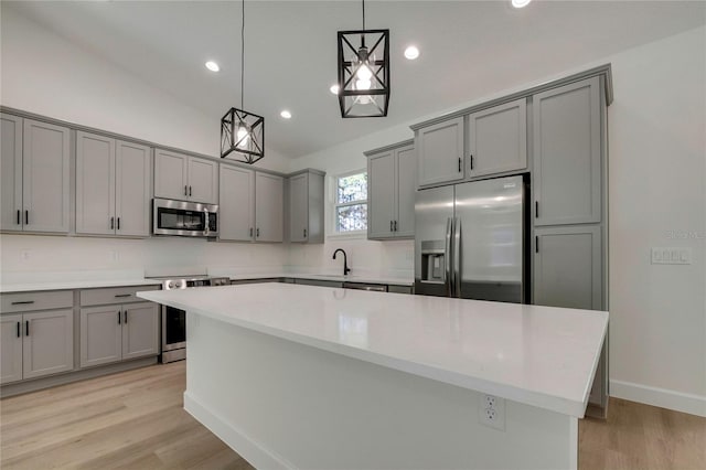 kitchen with gray cabinets, a kitchen island, stainless steel appliances, light hardwood / wood-style floors, and decorative light fixtures