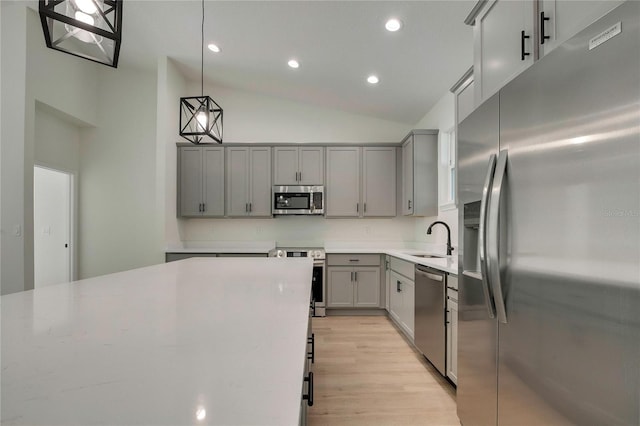 kitchen with appliances with stainless steel finishes, vaulted ceiling, sink, gray cabinetry, and decorative light fixtures