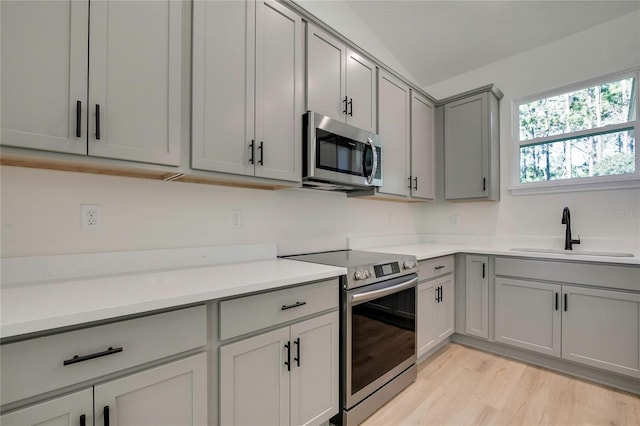 kitchen featuring lofted ceiling, sink, gray cabinets, appliances with stainless steel finishes, and light hardwood / wood-style floors