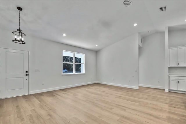 unfurnished living room with lofted ceiling, a chandelier, and light wood-type flooring