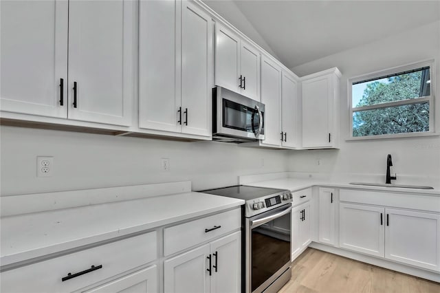 kitchen with stainless steel appliances, sink, vaulted ceiling, white cabinetry, and light hardwood / wood-style floors