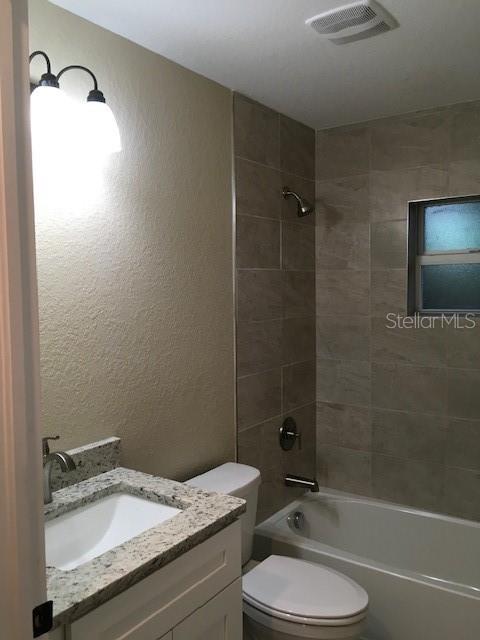 full bathroom featuring tiled shower / bath, vanity, and toilet