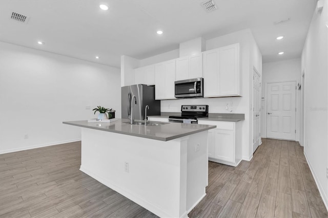 kitchen with an island with sink, sink, light wood-type flooring, white cabinetry, and appliances with stainless steel finishes