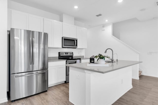 kitchen with appliances with stainless steel finishes, white cabinetry, a center island with sink, and light hardwood / wood-style floors