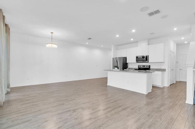 kitchen with white cabinets, a center island with sink, appliances with stainless steel finishes, light hardwood / wood-style flooring, and pendant lighting