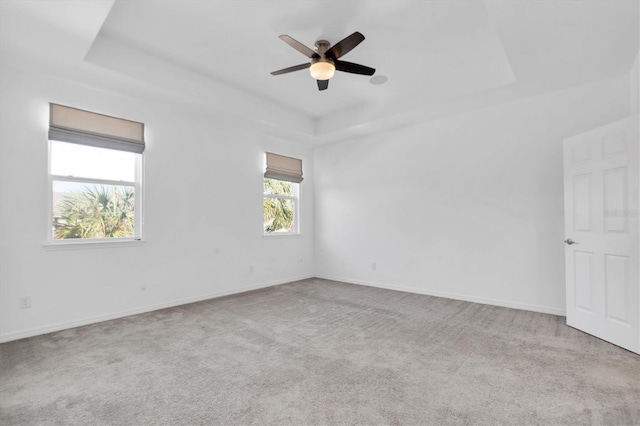 spare room with light carpet, a tray ceiling, and ceiling fan