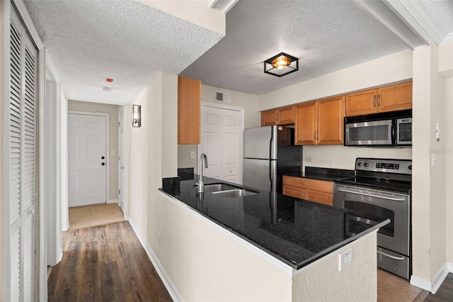 kitchen featuring dark hardwood / wood-style floors, kitchen peninsula, sink, appliances with stainless steel finishes, and a textured ceiling