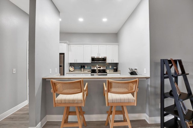 kitchen featuring stainless steel appliances, a kitchen bar, hardwood / wood-style floors, white cabinets, and decorative backsplash