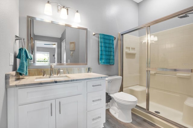 bathroom featuring toilet, vanity, wood-type flooring, and a shower with shower door