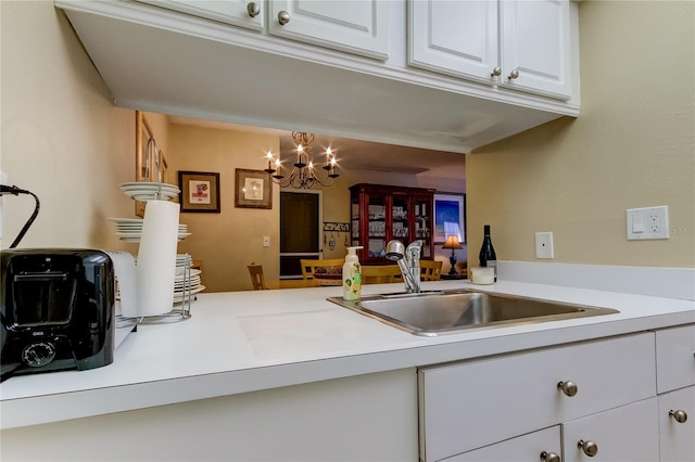 kitchen with sink, an inviting chandelier, and white cabinets