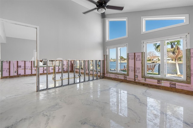 empty room featuring a high ceiling, ceiling fan, and a water view