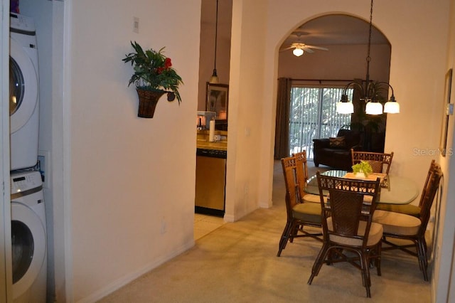 dining space featuring stacked washer / drying machine, light colored carpet, and ceiling fan with notable chandelier